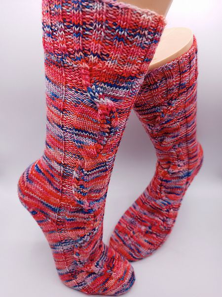 Mehrfarbige handgestrickte Socken mit Zopfmuster in Rot- und Blautönen vor hellem Hintergrund.