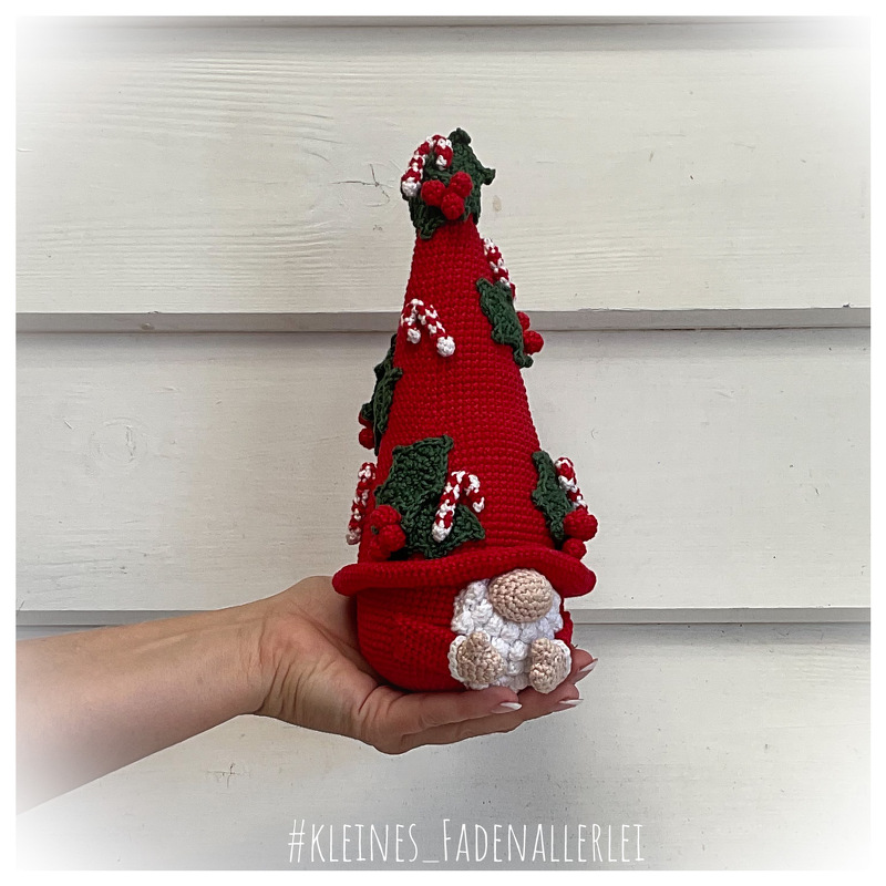 hand holding a small red crocheted gnome with holly leaves, red berries, candy canes and a white beard