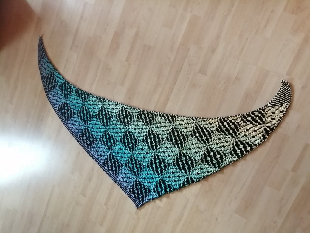 Gestricktes Dreieckstuch mit schwarz und türkis gemustertem Rautenmotiv auf Holzfußboden