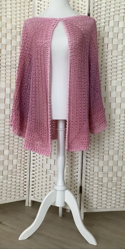 Helle rosa offene Häkeljacke auf einer weißen Schneiderpuppe mit luftigem Maschenmuster und gewelltem Saum.