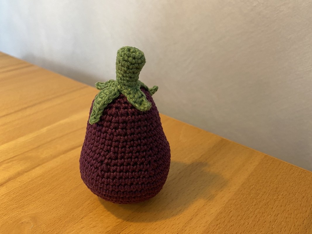Gehäkelte Aubergine auf einem Holztisch vor weißer Wand