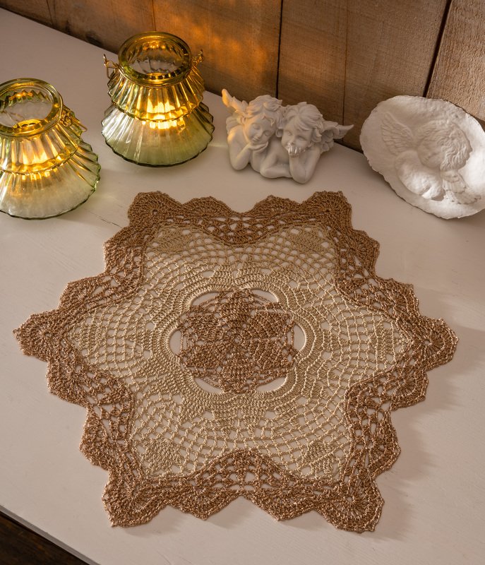 Handgehäkeltes sternförmiges Deckchen in Braun- und Goldtönen auf hellem Tisch, dekoriert mit goldenen Laternen und Engelsfiguren.