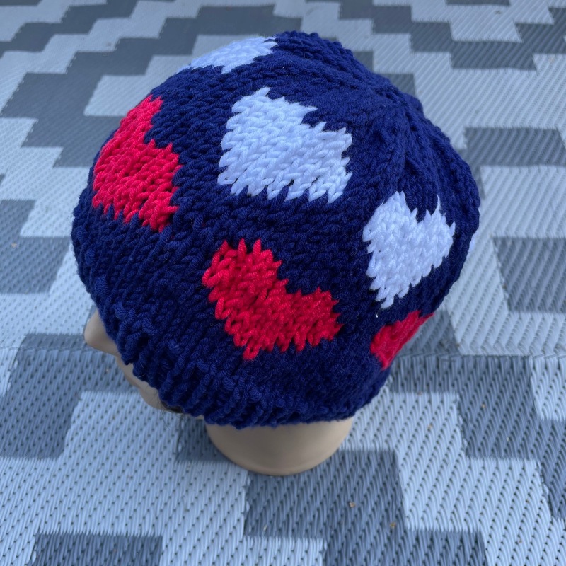 Dunkelblaue Strickmütze mit roten und weißen Herzmotiven auf einer Schaufensterpuppe