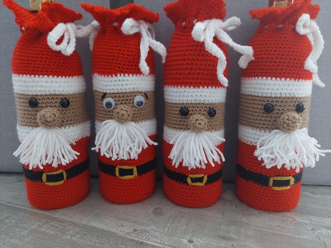 Vier gehäkelte Nikolaus-Flaschenhüllen in Rot, Weiß und Beige mit Bart und Gürtel.