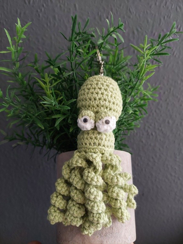 Hellgrüner gehäkelter Amigurumi-Oktopus-Schlüsselanhänger vor einer Zimmerpflanze