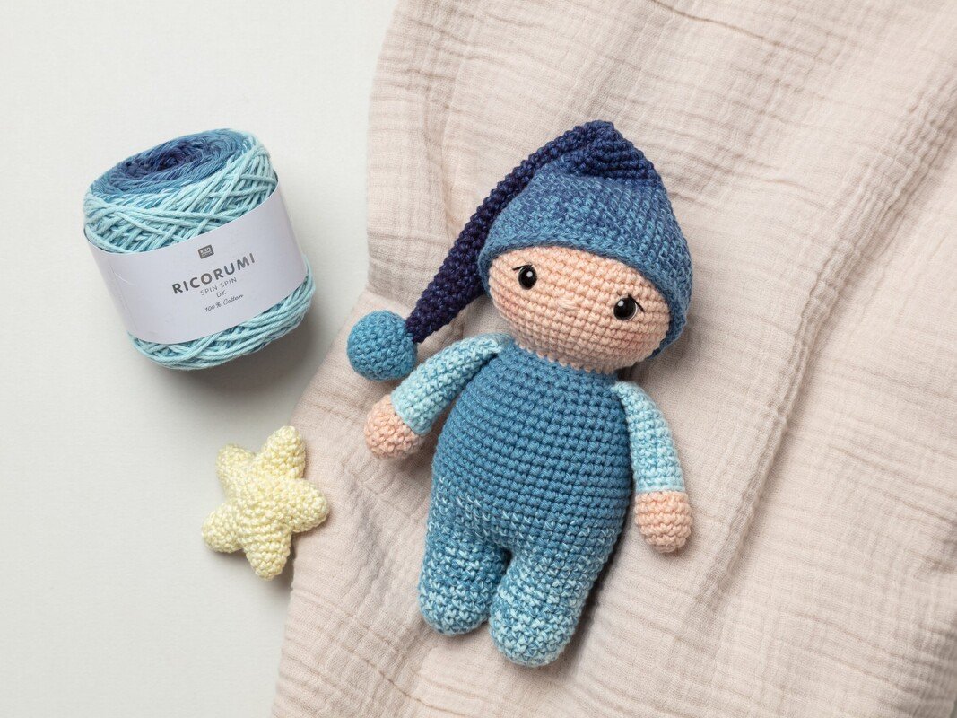 Gehäkelte Amigurumi-Schlafpuppe in Blautönen mit Zipfelmütze, daneben Knäuel Farbverlaufsgarn und gehäkelter Stern.