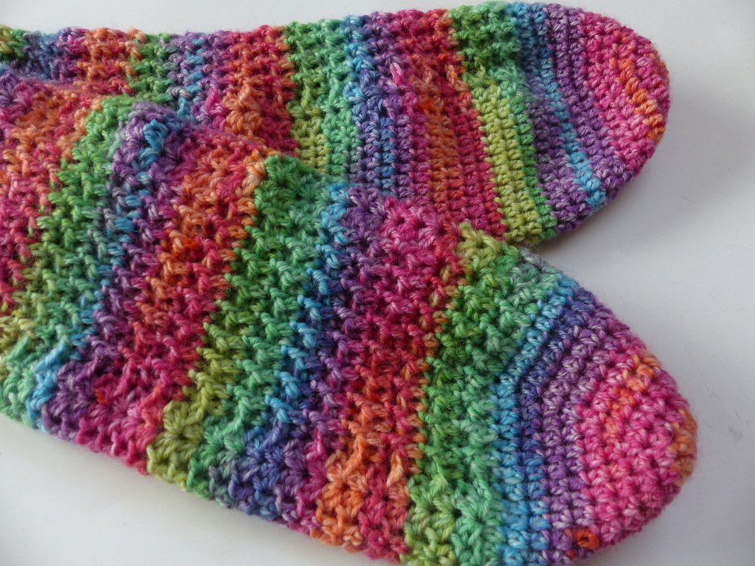 Nahaufnahme gehäkelte Socken in bunten Regenbogenstreifen mit strukturierter Maschenfolge und abgerundeter Spitze