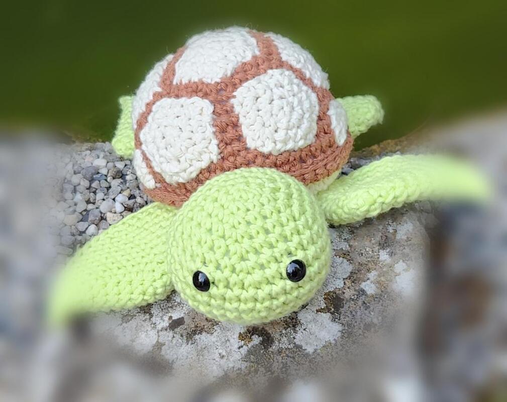 Gehäkelte Amigurumi-Schildkröte mit hellgrünem Kopf und weiß-braunem Panzer auf Stein