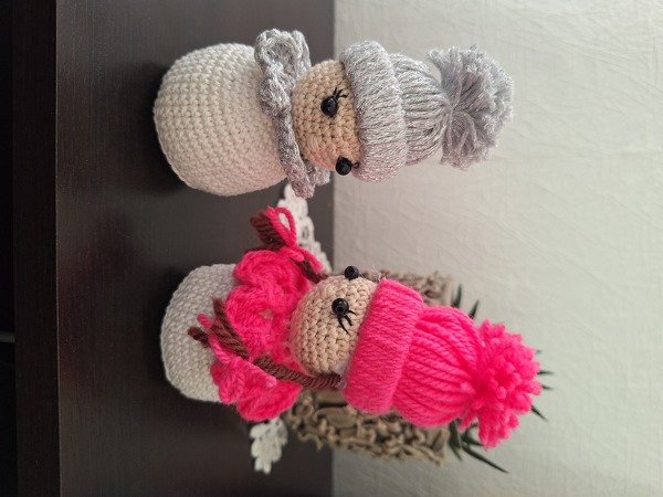 Zwei gehäkelte Engel‑Figuren mit Mützen und Flügeln, eine grau, eine pink.