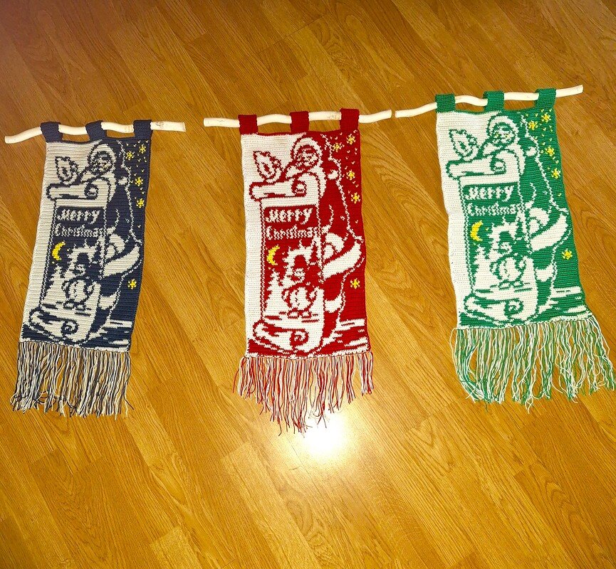 Drei handgearbeitete Häkelbanner in Blau, Rot und Grün mit traditionellem Weihnachtsmotiv, Fransen und Aufhängeschlaufen