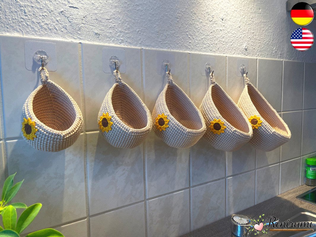 Five crocheted hanging baskets with sunflower appliqués hung on a tiled kitchen wall