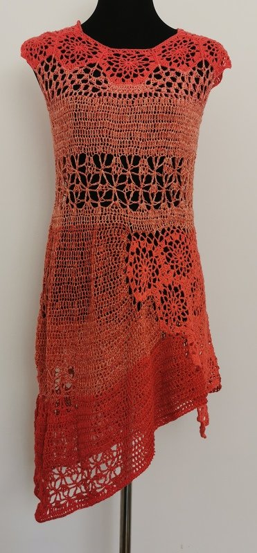 Gehäkelte korallfarbene Tunika mit runden Spitzen, Netzstreifen, floralen Motiven und schrägem Saum auf einer Schaufensterpuppe