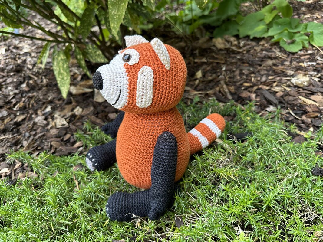 Handgehäkelter roter Panda Amigurumi sitzt auf moosigem Boden