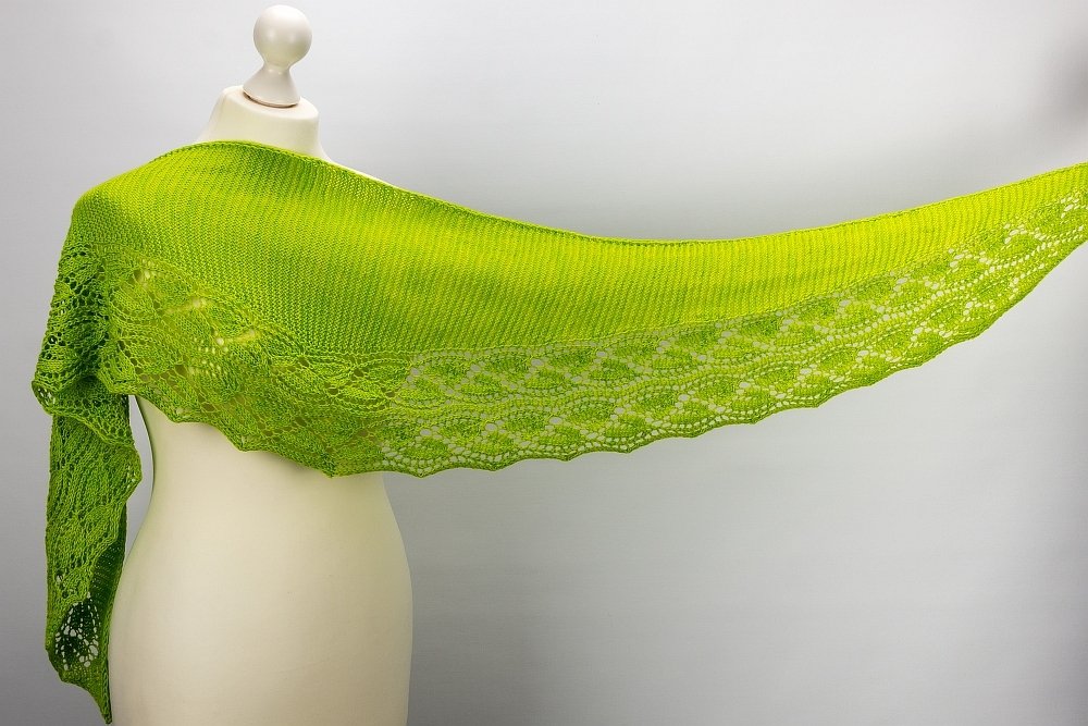 Bright green knitted shawl with decorative lace border and scalloped edge draped on a white mannequin.
