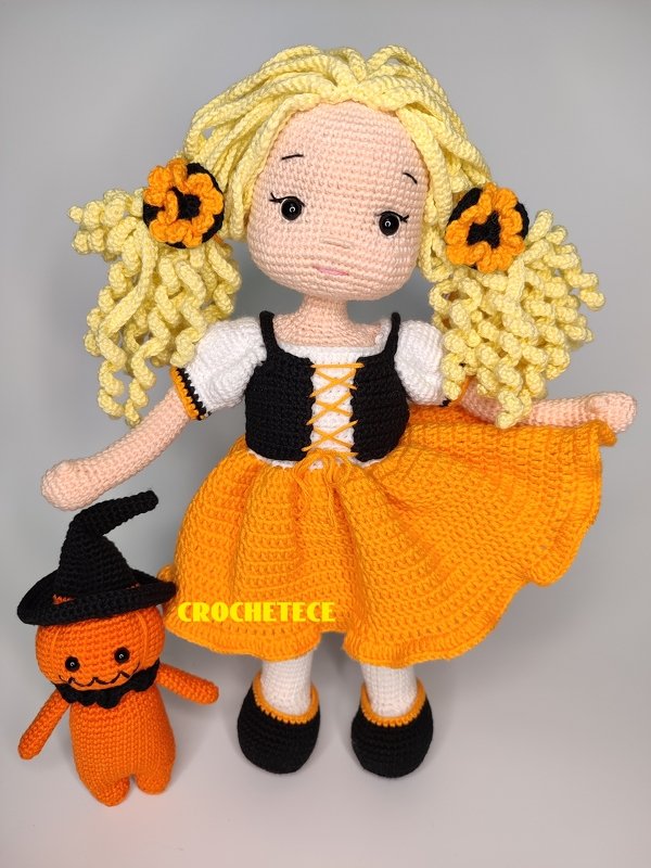 Crochet amigurumi doll with orange skirt, curly blonde pigtails, and small pumpkin plush in witch hat