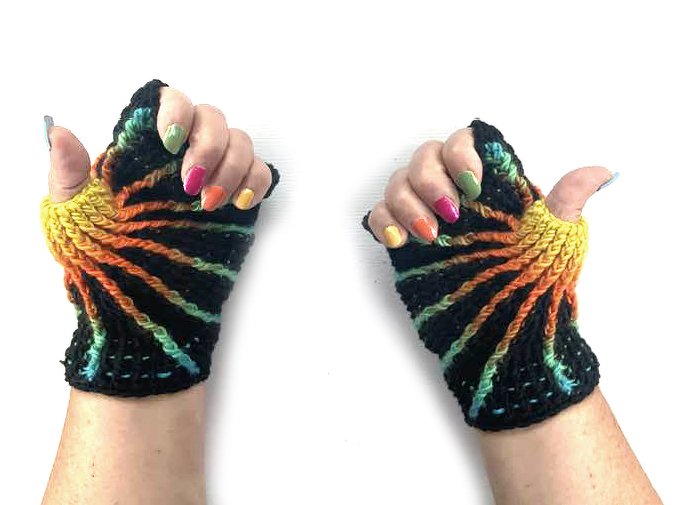 Zwei Hände mit gehäkelten, fingerlosen Handschuhen in Schwarz und strahlenförmigen Regenbogenstreifen, Daumenöffnung sichtbar.