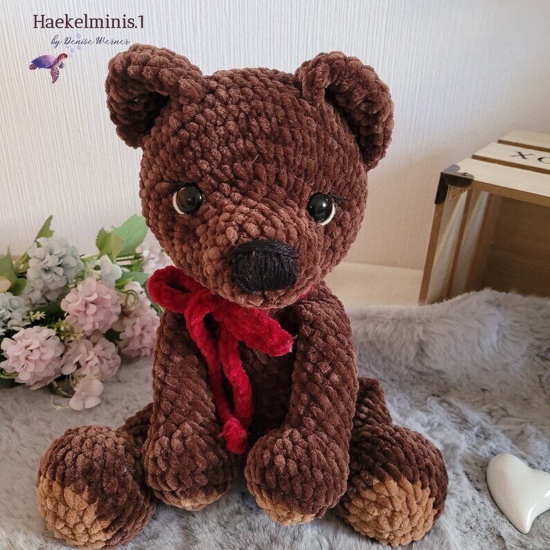 Sitzender gehäkelter Amigurumi-Teddybär in Braun mit roter Schleife