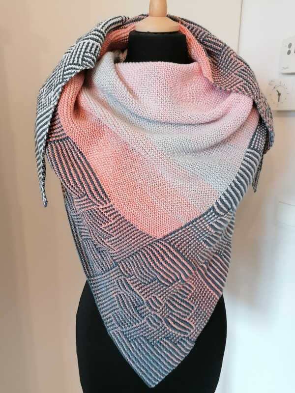 Gestricktes Dreieckstuch in Rosa und Grau mit geometrischem Strukturmuster auf einer Schneiderpuppe.