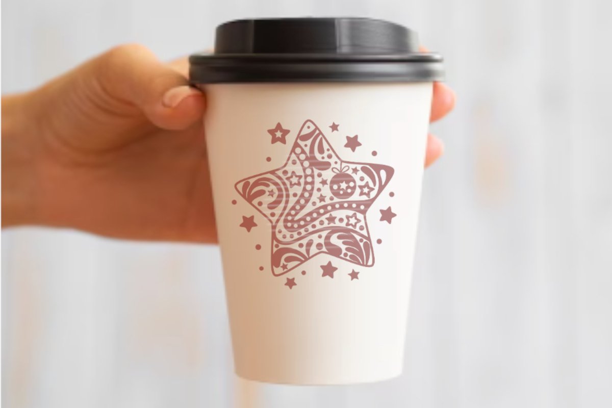 Weißer To-Go-Becher mit braunem ornamentalem Sternmotiv, gehalten in einer Hand