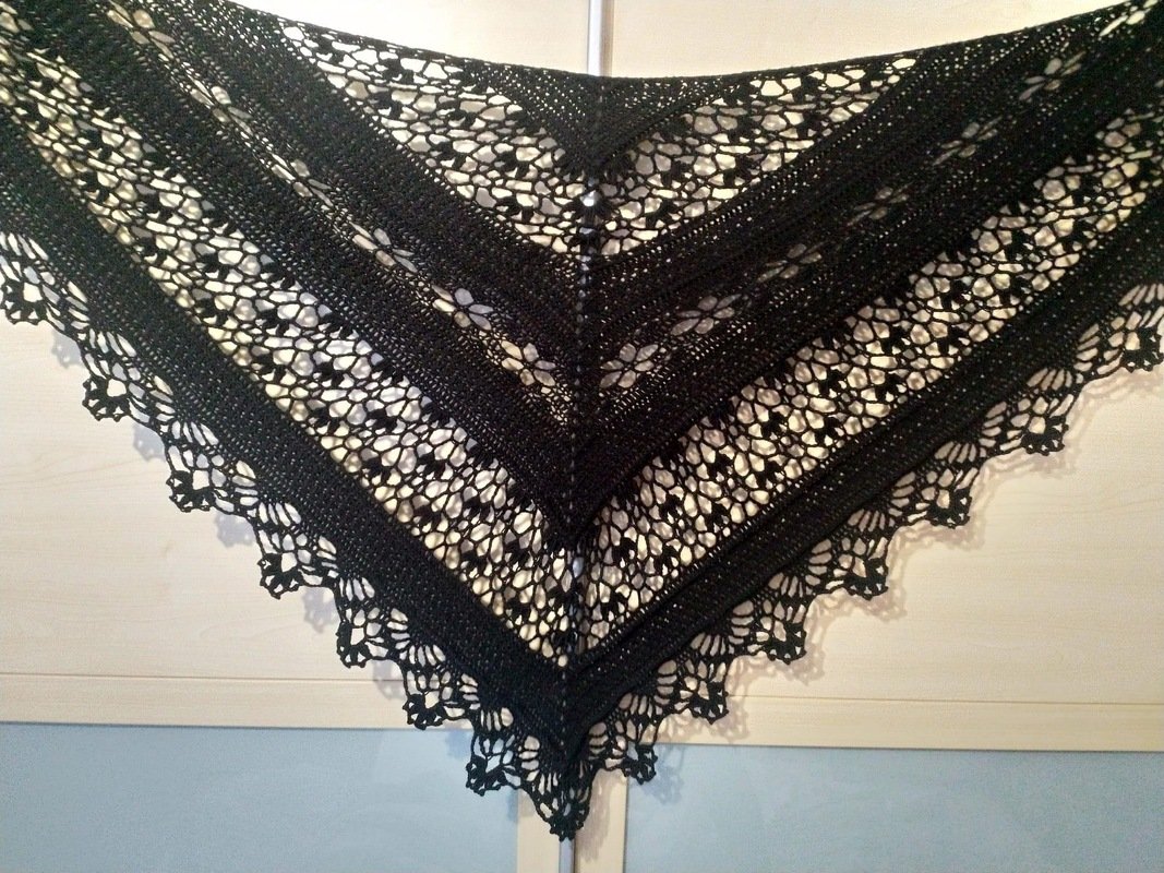 Black crocheted triangle shawl with alternating lace and solid bands and a scalloped border.