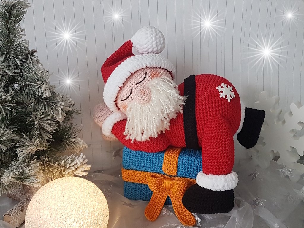 Gehäkelter Weihnachtsmann liegt auf einer blauen Geschenkbox neben weihnachtlicher Deko