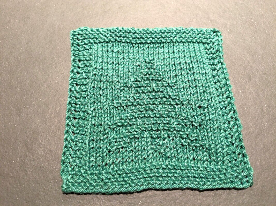 Quadratischer, türkisgrüner Strickuntersetzer mit Tannenbaum-Relief auf dunklem Hintergrund