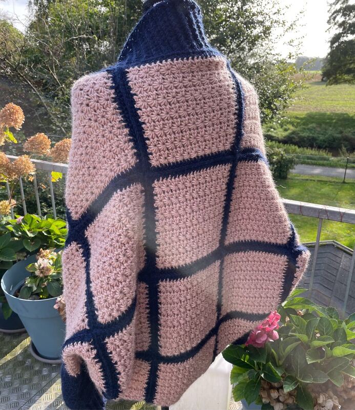 Gehäkelter Seelenwärmer in Rosa mit dunkelblauem Gittermuster auf einem Balkon