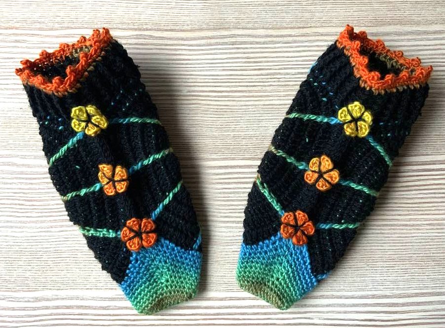 Paar schwarze gehäkelte Damen-Stulpen mit grünen Schrägstreifen, bunten Blüten und blau-grünem Fußbereich