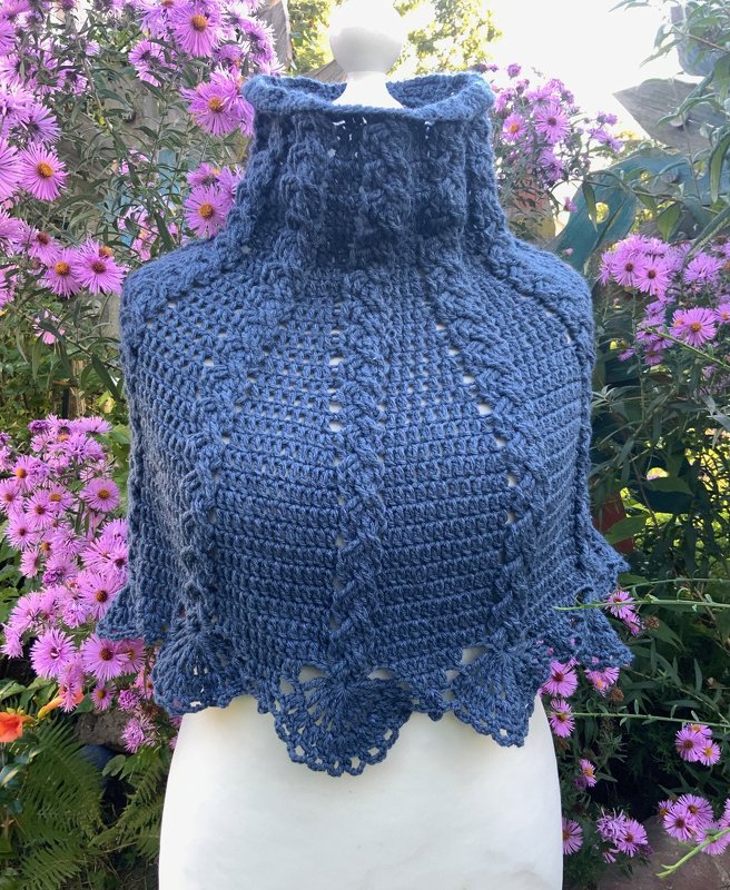 Blauer gehäkelter kurzer Schal mit hohem Kragen auf Schaufensterpuppe vor Blumen