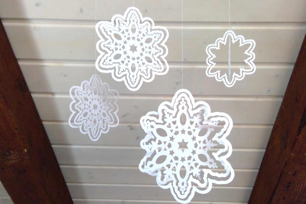 Verschiedene ornamental gestaltete Schneeflocken mit feinen Ausschnitten, an transparenten Fäden befestigt