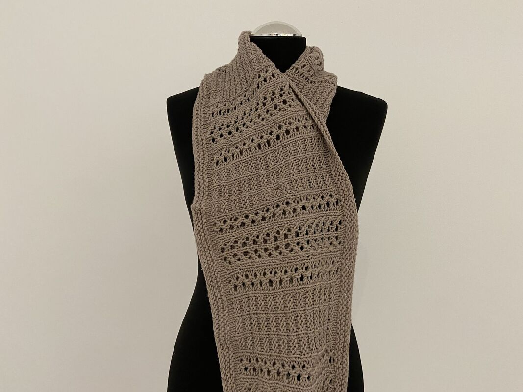 Schmaler gestrickter Loop-Schal in Taupe mit Loch- und Rippenstreifen, drapiert an einer schwarzen Schaufensterpuppe
