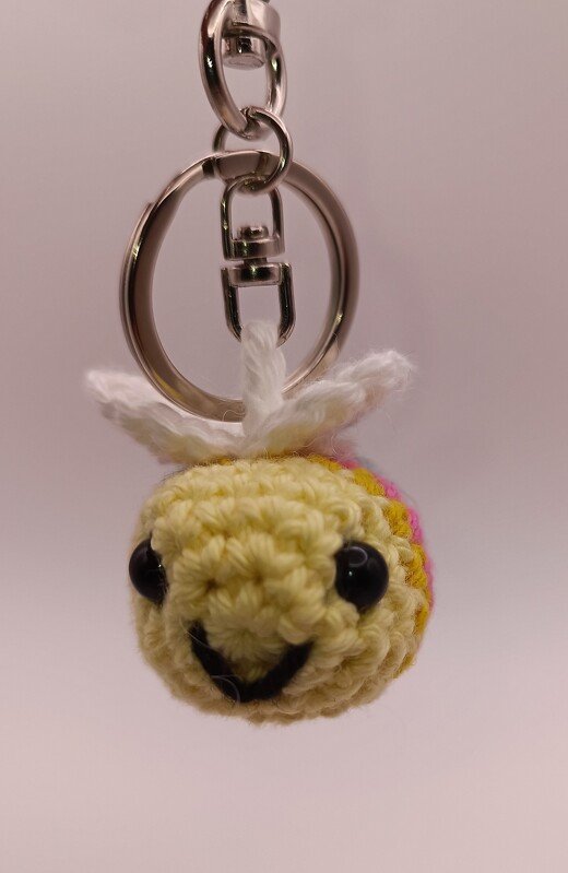 Handgehäkelter gelber Amigurumi-Glücksbringer mit weißen Flügeln an Metallring