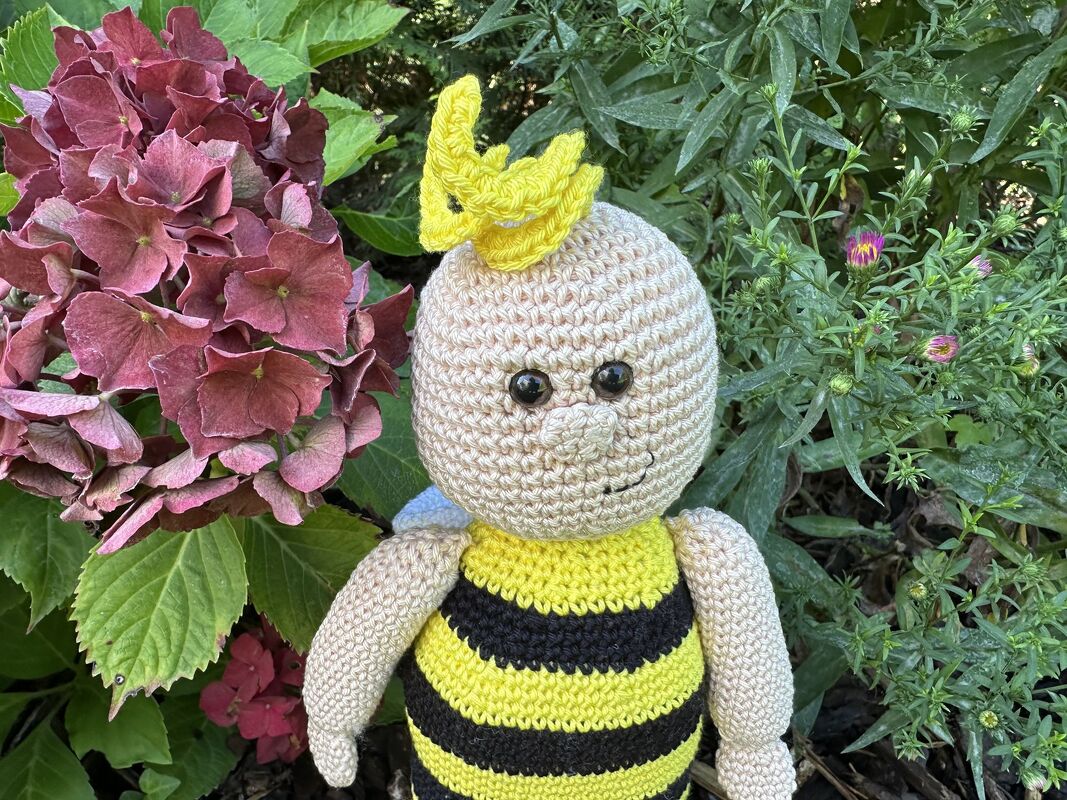 Gehäkeltes Amigurumi-Bienchen mit gelb-schwarzen Streifen und gelbem Haarschopf neben einer Hortensie