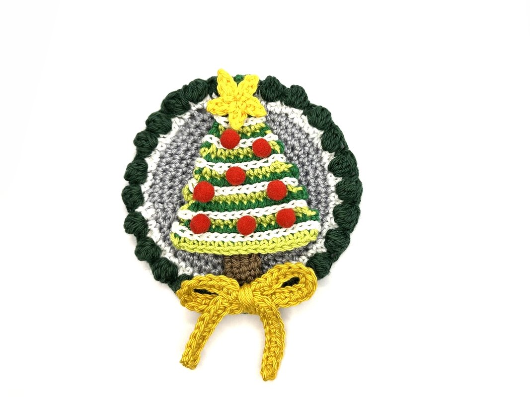 Round crocheted Christmas tree appliqué with red pom-poms, yellow star and yellow bow on grey background with green scalloped edge.