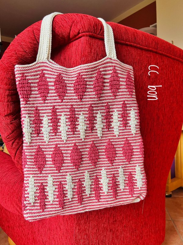 Gehäkelte Henkeltasche in Rosé und Beige mit Rautenmuster auf rotem Sessel