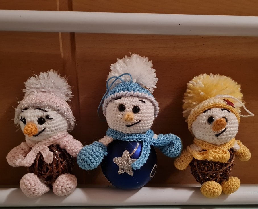 Drei gehäkelte Schneemann-Amigurumis, einer mit blauer Christbaumkugel als Körper