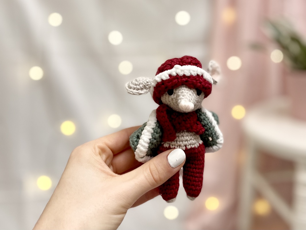 Gehäkelte Amigurumi‑Maus mit roter Mütze und Schal vor warmen Lichterpunkten