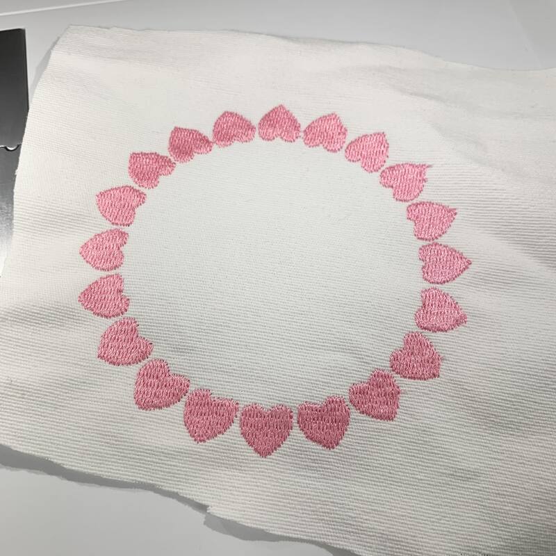 Kreisförmiger Rahmen aus rosa Herzen, auf hellem, strukturiertem Stoff gestickt