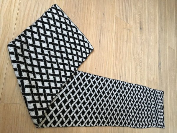 Schwarz-weißer gestrickter Schal mit diagonalem Gittermuster auf hellem Holzfußboden