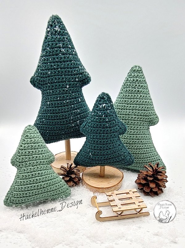 Vier gehäkelte Weihnachtsbäume in unterschiedlichen Grüntönen und Größen auf Holzscheiben, mit Kunstschnee, Tannenzapfen und einem kleinen Holzschlitten.
