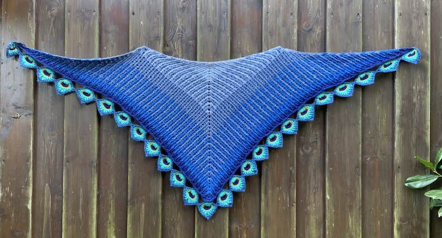 Gehäkeltes blaues Dreieckstuch mit türkiser Muschelkante an einem Holzzaun
