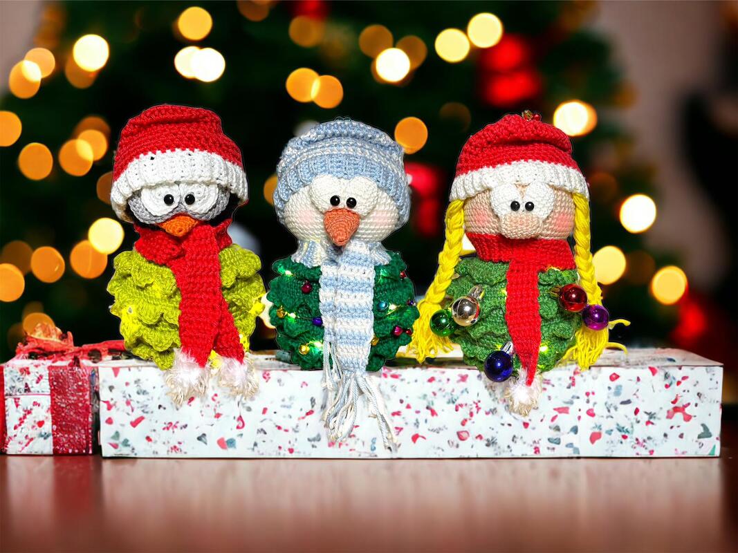 Drei gehäkelte Weihnachts-Amigurumi mit Mützen, Schals und Kugeln vor Lichterbokeh