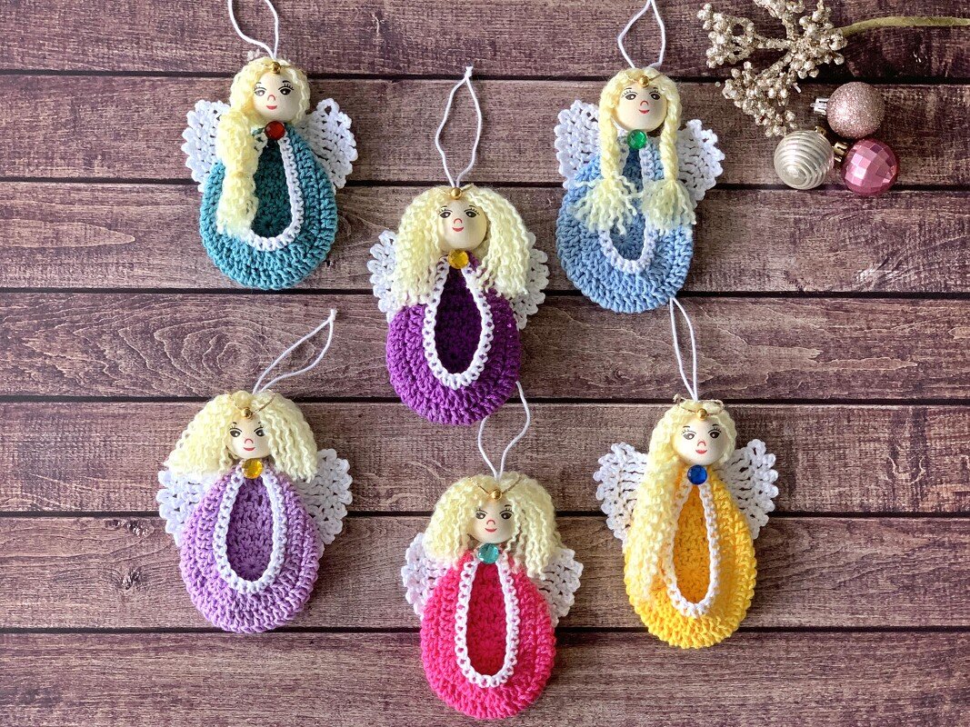 Handgearbeitete gehäkelte Engel-Ornamente in Reihe auf Holzhintergrund, jede in einer anderen leuchtenden Farbe.