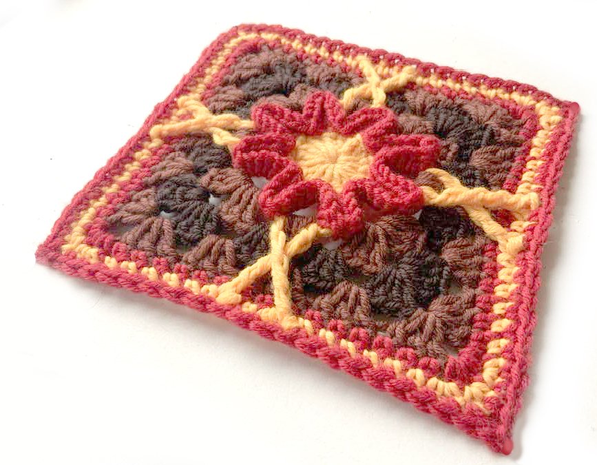 Gehäkeltes Granny Square mit gelber Mitte, roten Rüschen und braunem Hintergrund