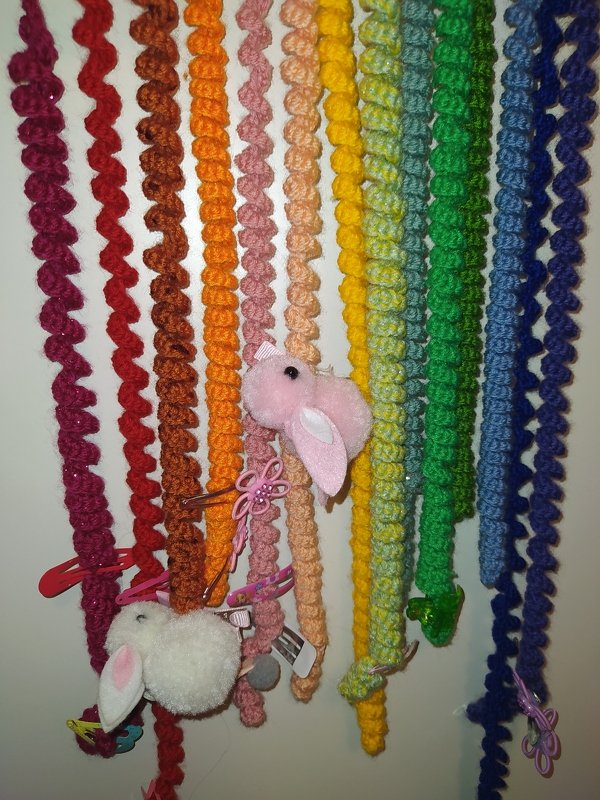 Gehäkelte Regenbogenstränge mit daran befestigten Haarspangen und kleinen Plüschhasen