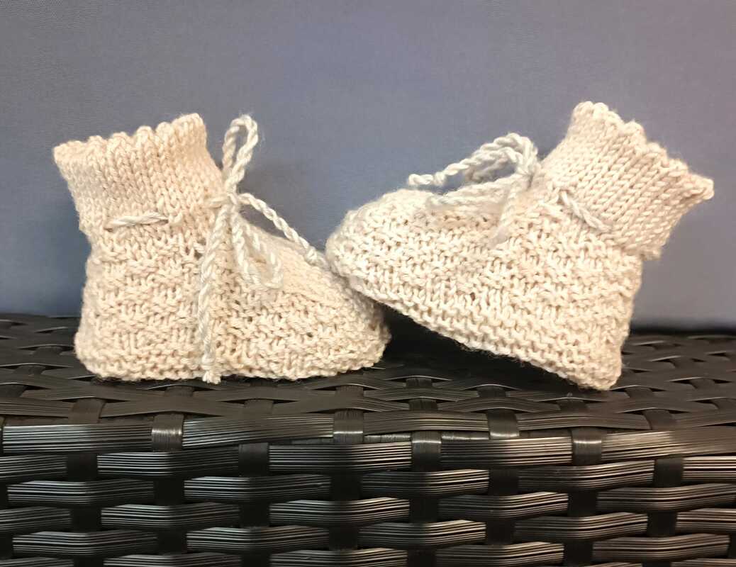 Zwei handgestrickte hellbeige Babyschuhe mit Bindebändern auf dunklem Untergrund