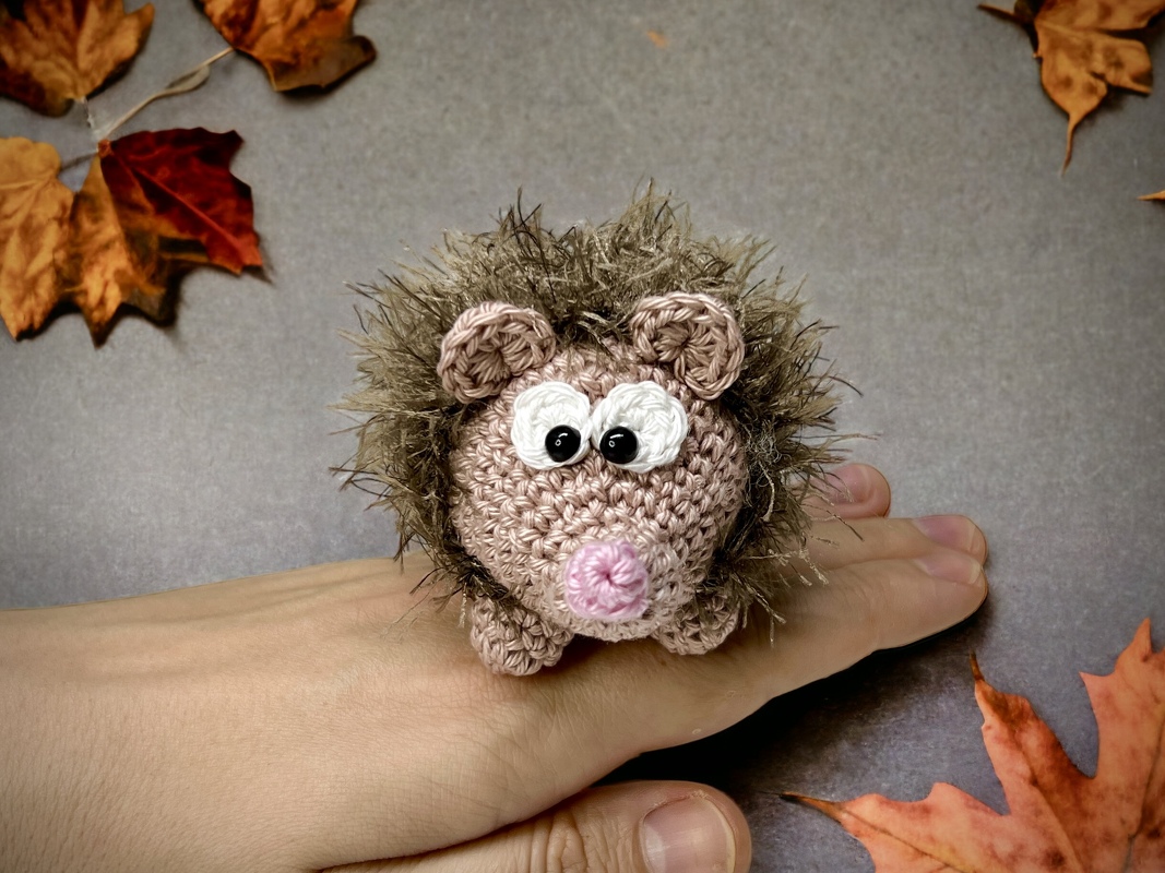 Mini Amigurumi Igel auf einer Hand zur Größenvorstellung, detailreiches Gesicht und flauschige Stacheln