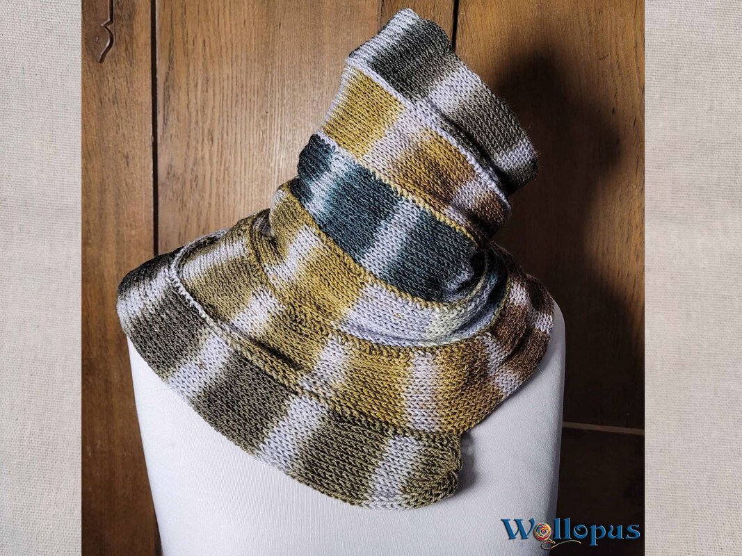 Gestrickter Loop-Schal in Olivgrün, Senfgelb und Hellgrau mit Karomuster auf einer weißen Schneiderpuppe.