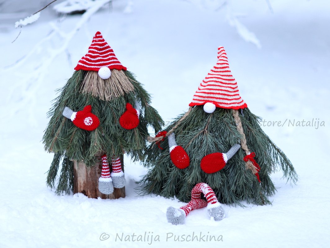 Zwei Weihnachtswichtel aus Tannenzweigen mit rot-weiß gehäkelten Mützen und Fäustlingen im Schnee