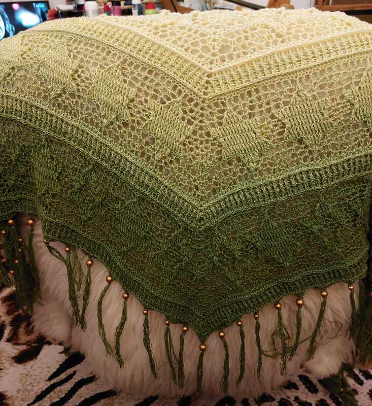 Ombre green crochet triangle shawl with lace stitches and beaded tassels on white faux fur.